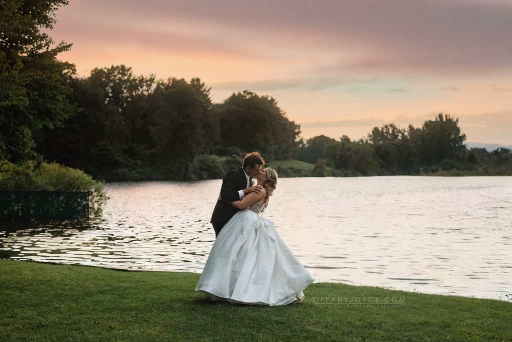 bride and groom kissing at sunset in front of lake over country club of pittsfield wedding