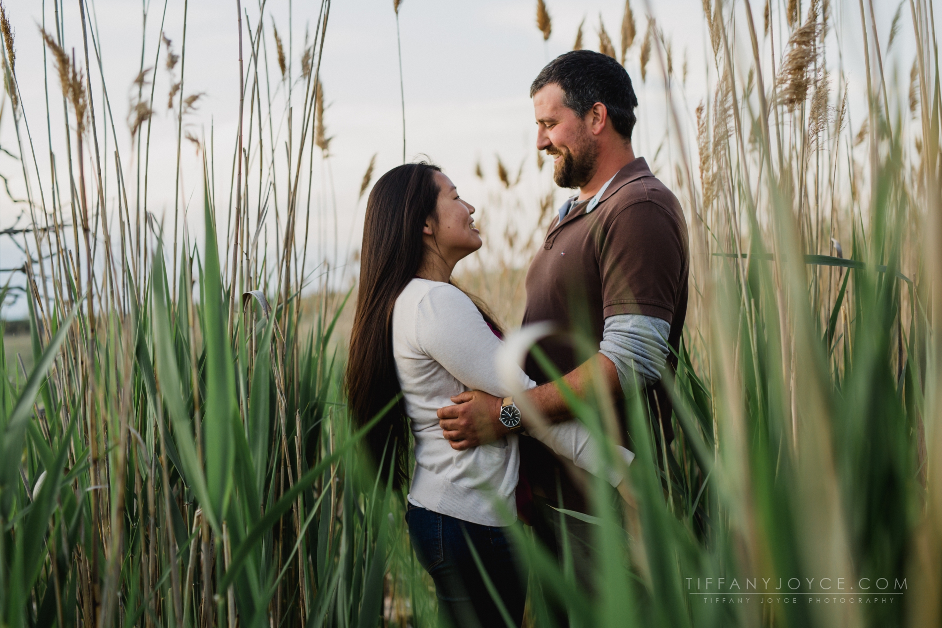 Couple embracing in beach grass during Madison engagement session in CT